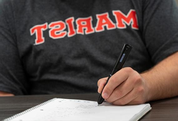 Image of a student with pen writing on notebook paper.