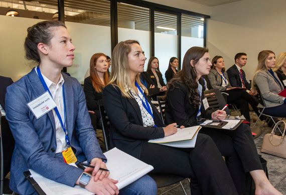 Image of students taking notes at a business presentation.